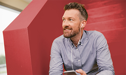 Man sitting on red staircase, listening to a podcast with headphones