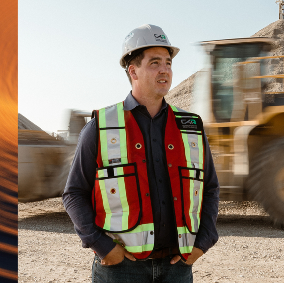 Travis Powell wearing protective gear and walking in aggregate field with tractors whizzing by