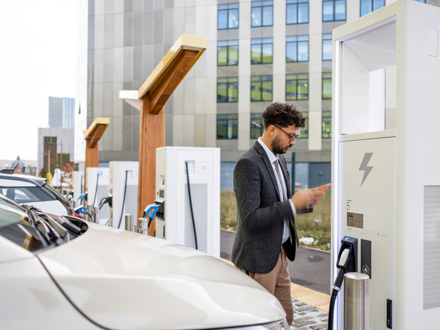 Man looking at his cell phone while charging his e-vehicle