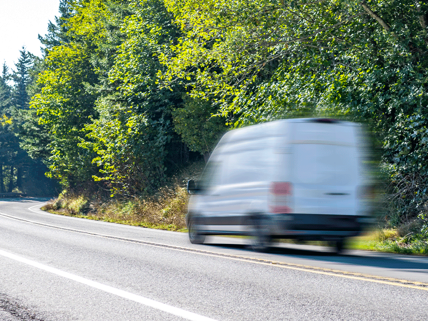 White cargo van on a road next to a forest