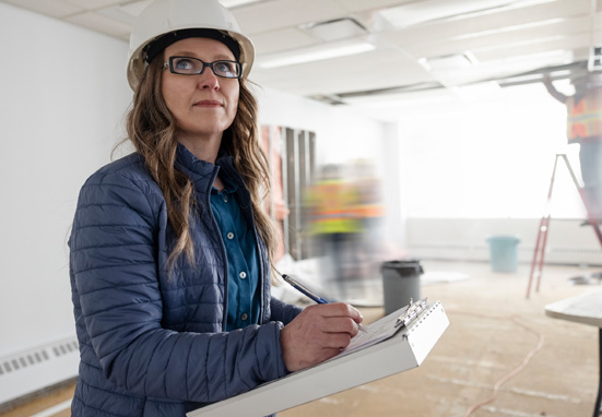 woman in hard hat writing notes on construction site with workers in the background