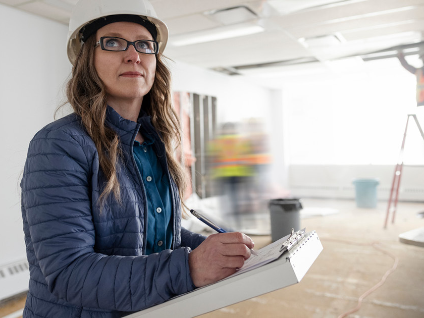 woman in hard hat writing notes on construction site with workers in the background