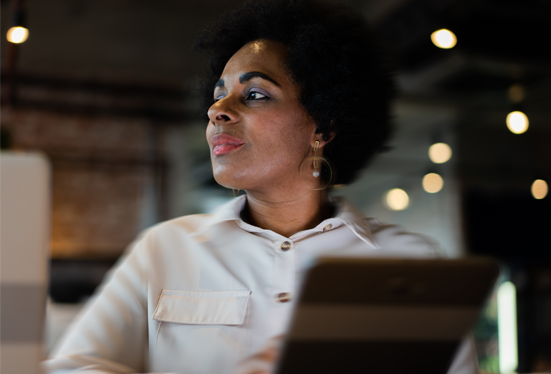 black woman looking to the side, holding a tablet in a dark and modern office environment