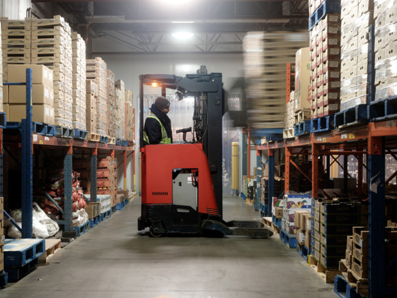 Warehouseman wearing fluorescent yellow safety jacket and driving a red forklift in a warehouse.