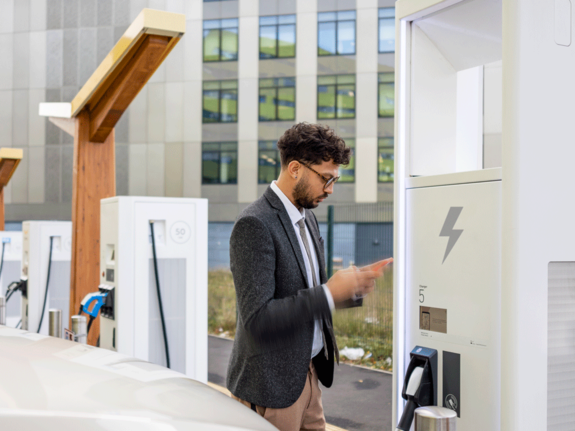 Man looking at his cell phone while charging his e-vehicle