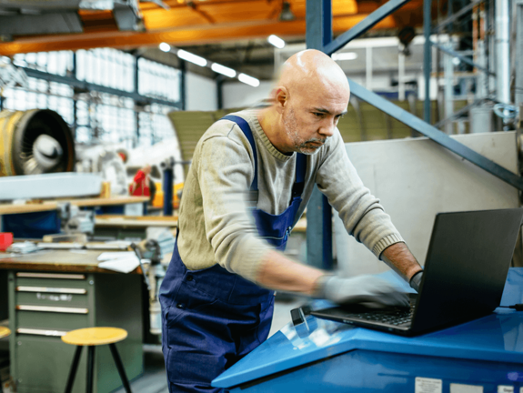 man in overalls in a factory, working on a laptop